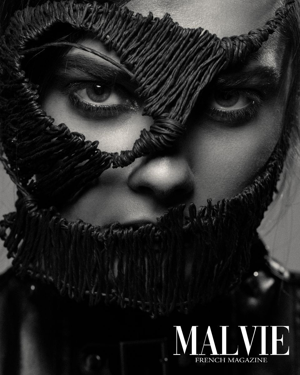 Close-up black-and-white portrait of a woman with dark hair, striking eyes, and decorative black fringe covering part of her face.
