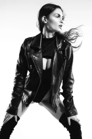 Model wearing a black leather jacket and thigh-high boots against a bright white background, photographed by Geoffrey Badner