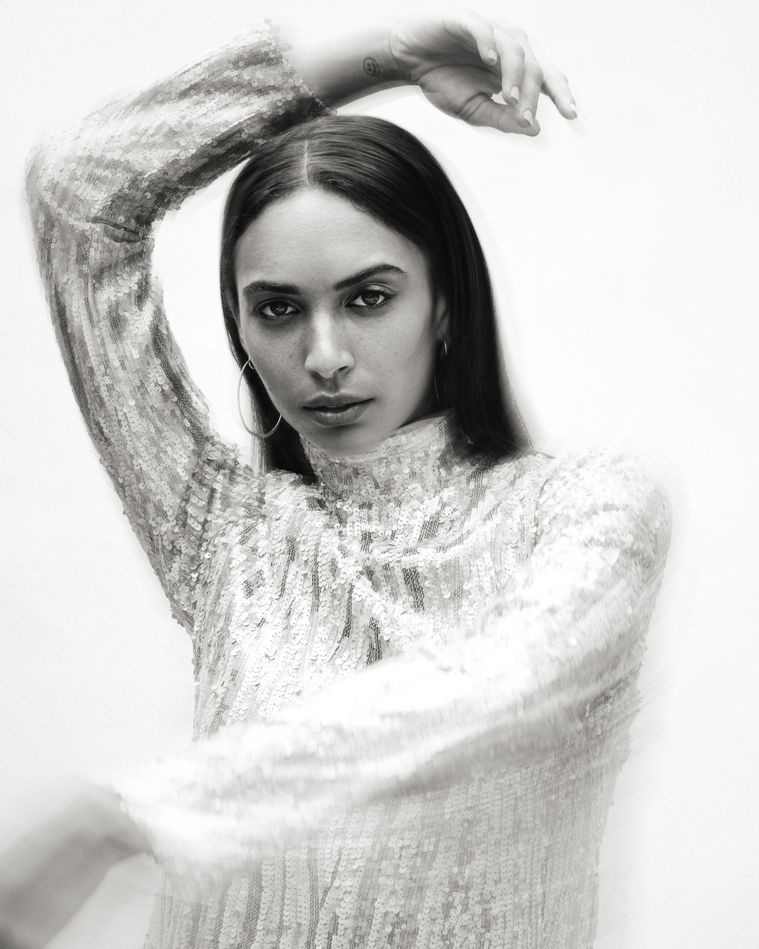 Monochrome portrait of a woman in a sequined top, gazing directly at the camera with soft-focus and shallow depth of field.