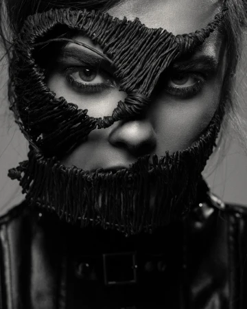 Striking black and white portrait of a woman with intricate thread mask, eyes focused, in a studio setting with soft lighting.