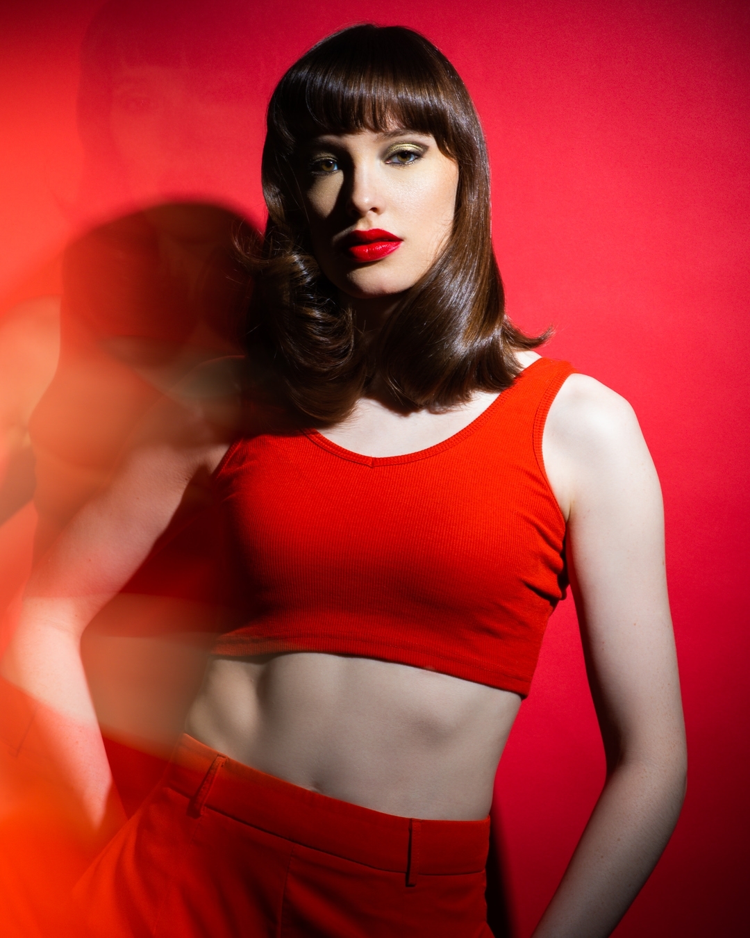 A woman with red lipstick and a red outfit poses against a vibrant red background in a studio setting with dynamic lighting.