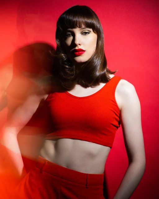 A woman with red lipstick and a red outfit poses against a vibrant red background in a studio setting with dynamic lighting.