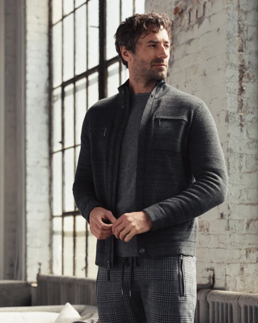 Adult male posing in gray jacket and plaid pants indoors near a window, showcasing contemporary men's fashion.
