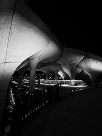 Black and white photo of the Little Island park in New York City, featuring its unique architecture and illuminated pathway along the water.