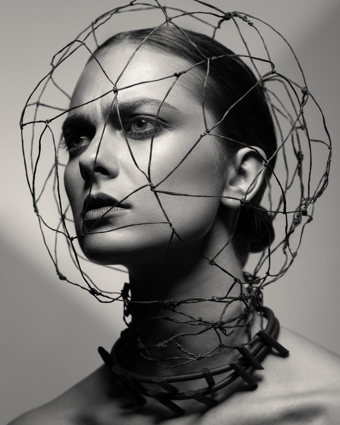 Monochrome portrait of a woman with artistic headpiece and statement necklace, captured in a studio with soft, diffused lighting.