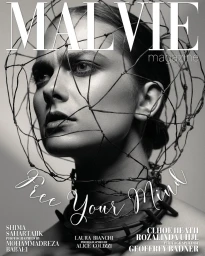 Close-up black and white portrait of a model with a dark sculptural wire structure framing her head and neck, photographed by Geoffrey Badner.