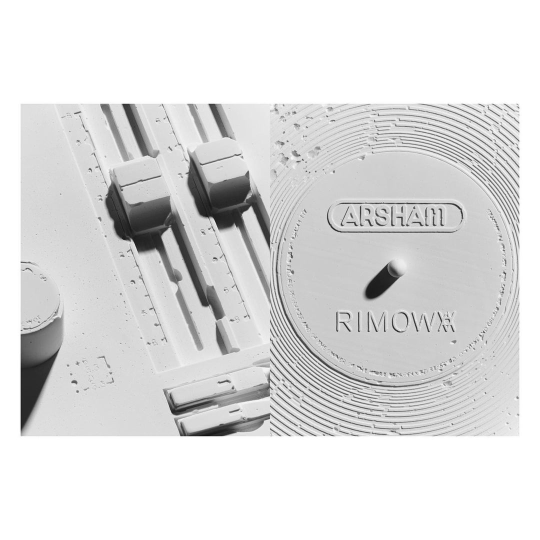 Monochromatic close-up of white sculptural objects: a mixing console segment with sliders and a circular form with raised lettering.