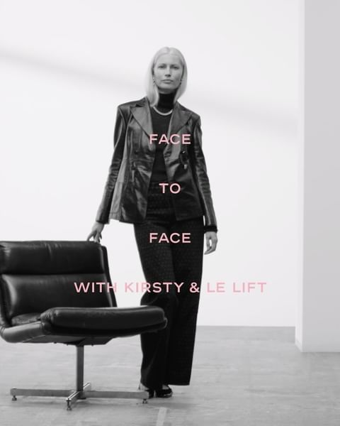 Elegant woman in a black blazer and wide-leg pants poses in a bright, minimalist photo studio with a black swivel chair.