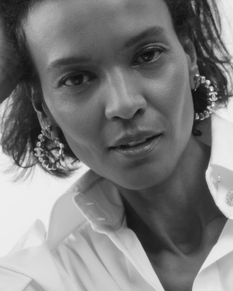 Black and white headshot of an adult woman with dark hair, hoop earrings, and a white collared shirt in an indoor setting.