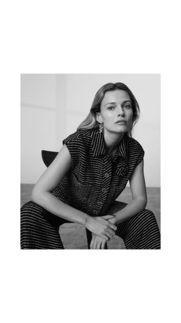 Black and white portrait of a woman with long hair wearing a striped top and pants, seated in a studio environment.
