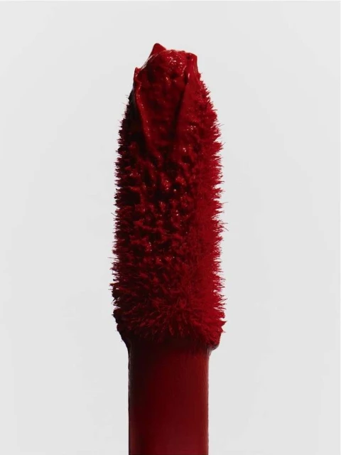Close-up of a red-pigmented lipstick applicator against a bright white backdrop, highlighting its texture and color.