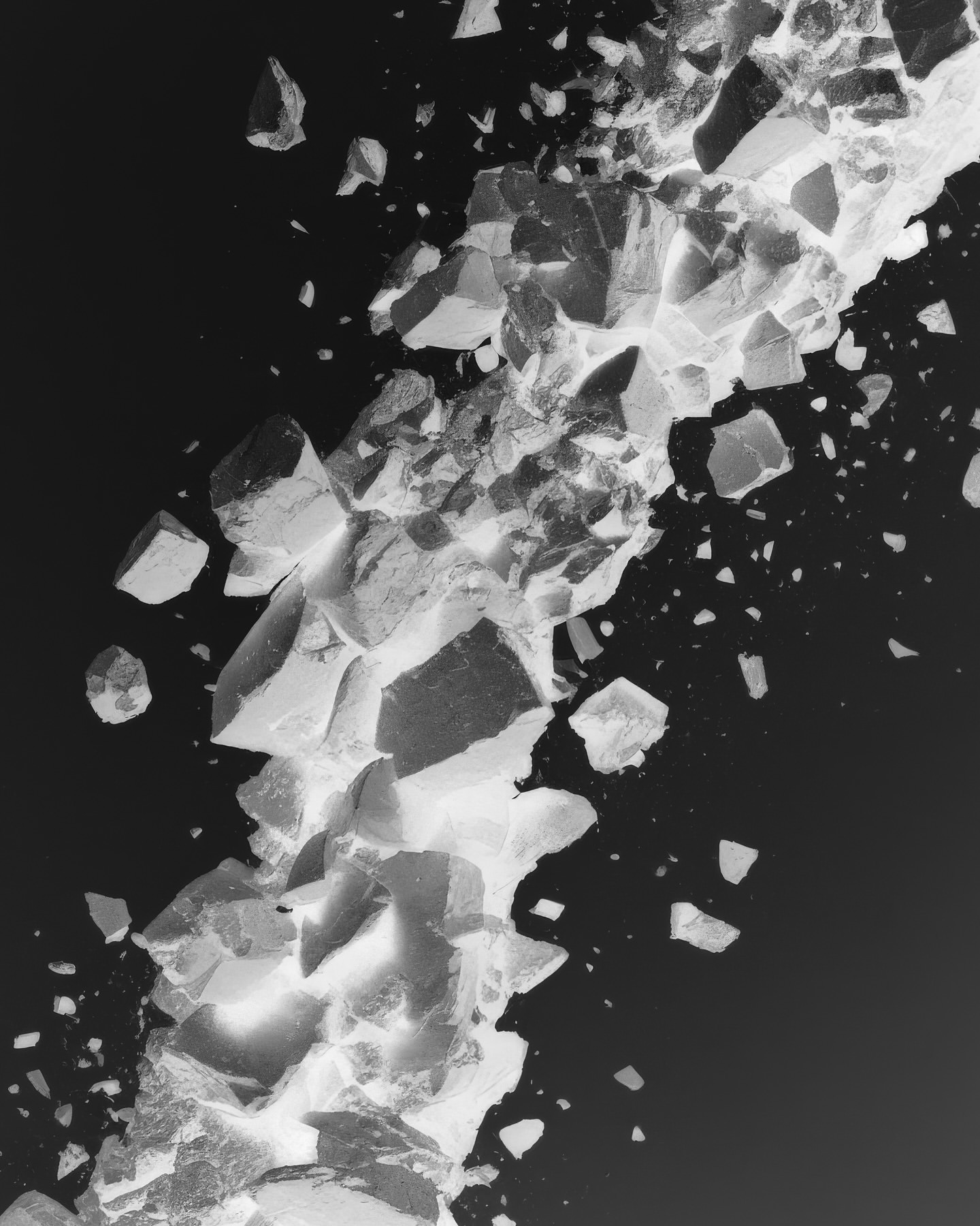 Monochromatic abstract composition featuring irregularly shaped rock fragments of varying sizes scattered on a stark black background.