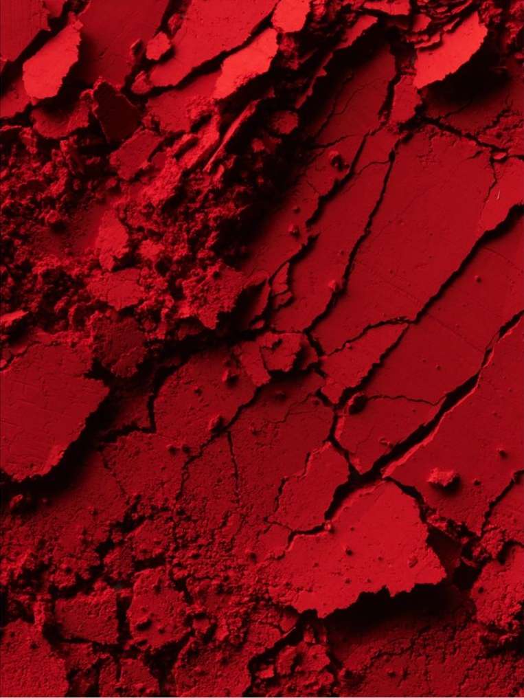 Close-up of red powder with cracked and crumbled texture. The monochromatic image shows variations in tone and shadow.