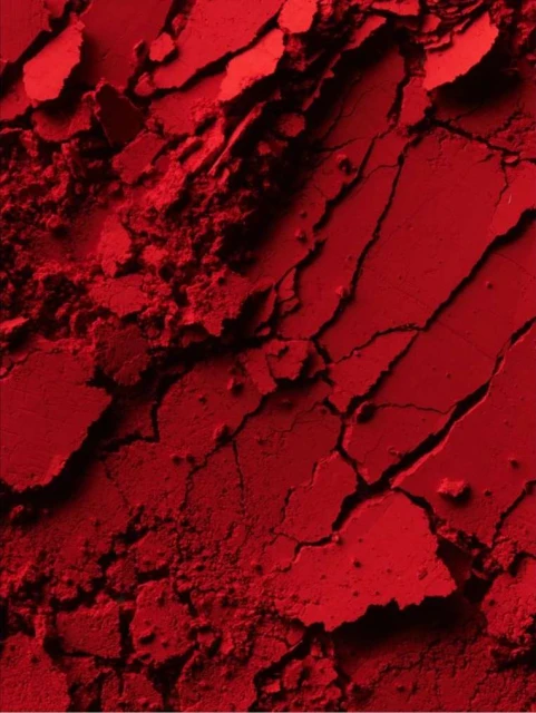 Close-up of red powder with cracked and crumbled texture. The monochromatic image shows variations in tone and shadow.