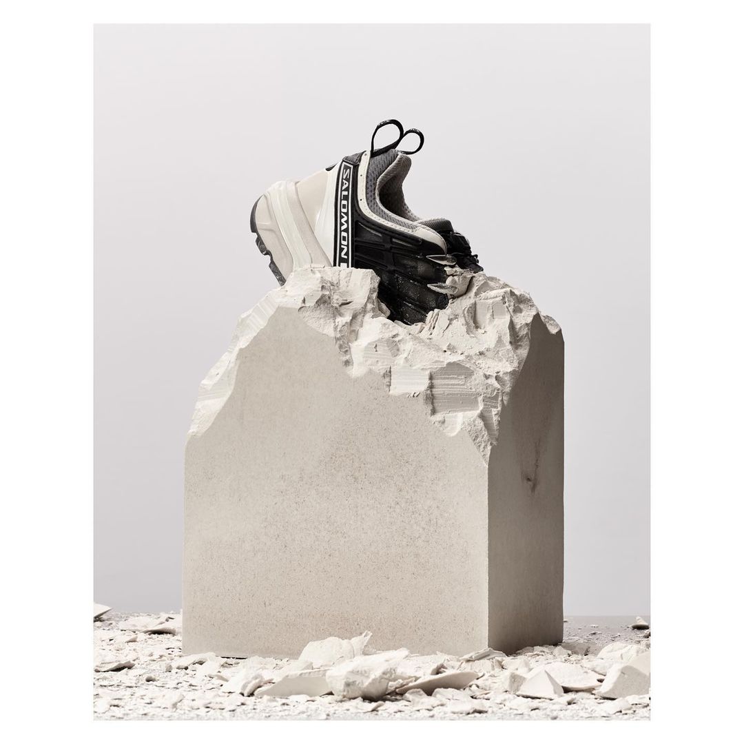 Salomon sneaker on a jagged concrete block in a studio setting. The athletic shoe is centered against a gradient white backdrop.