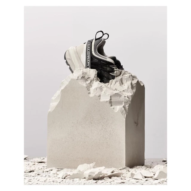 Salomon sneaker on a jagged concrete block in a studio setting. The athletic shoe is centered against a gradient white backdrop.