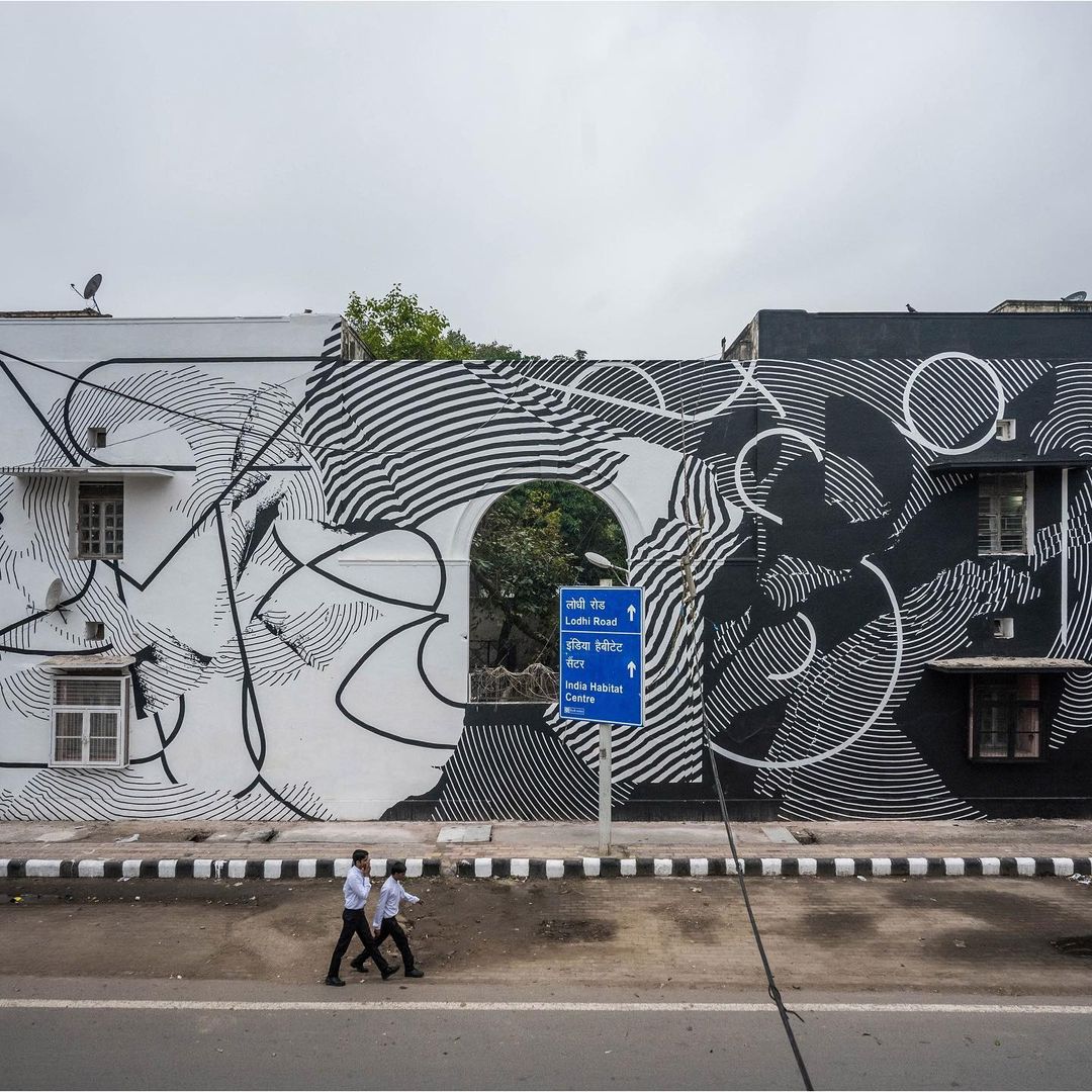Urban street art featuring abstract black and white designs on buildings, with two pedestrians walking along the road in daytime.