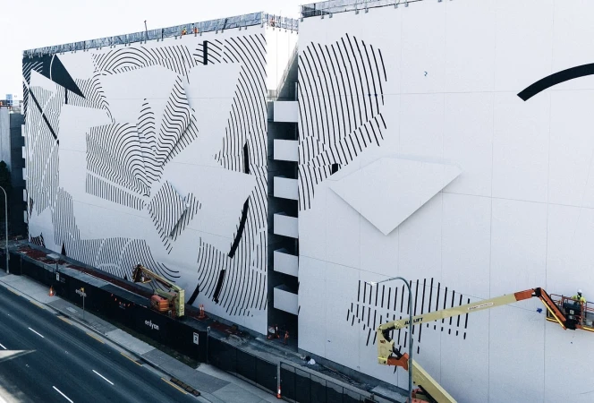 Exterior of a building featuring a black and white geometric mural, with construction and maintenance workers using a lift platform.