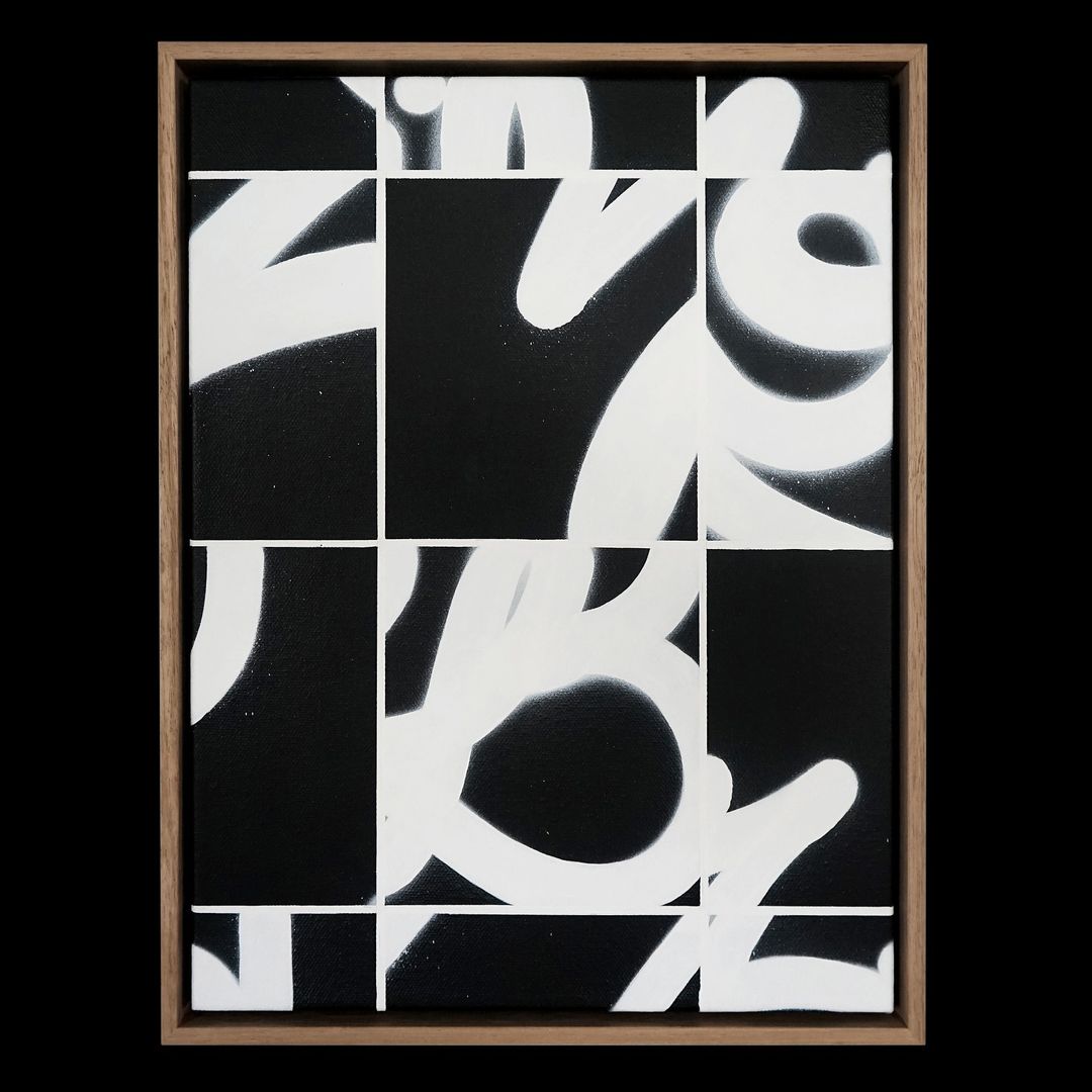 Abstract art in black and white with bold, stylized letterforms, presented in a light wood frame against a dark background.