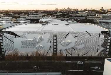 Aerial view of a large building facade featuring a vast monochrome geometric mural with curving lines by illustrator Georgia Hill.