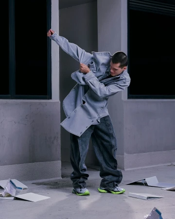 A male fashion model strikes a dynamic pose wearing a light blue denim jacket and dark jeans in an urban environment.