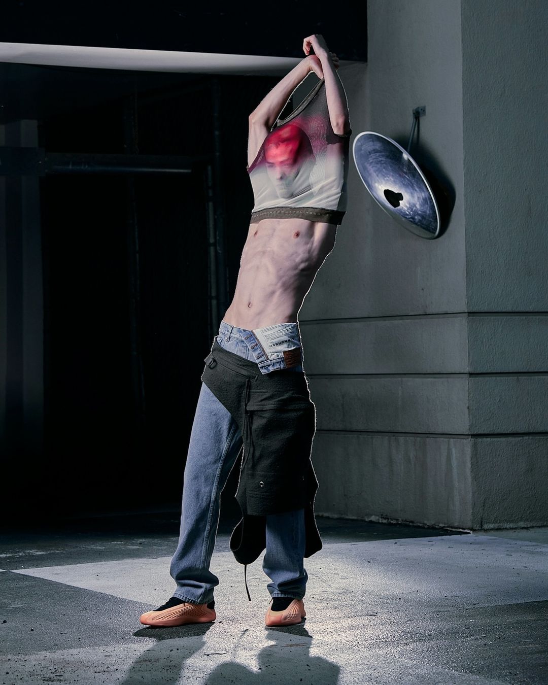 Adult male in casualwear pulling a t-shirt over his head outdoors in an urban environment with dim lighting and neutral color palette.