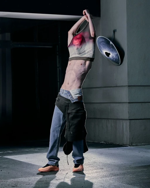 Adult male in casualwear pulling a t-shirt over his head outdoors in an urban environment with dim lighting and neutral color palette.