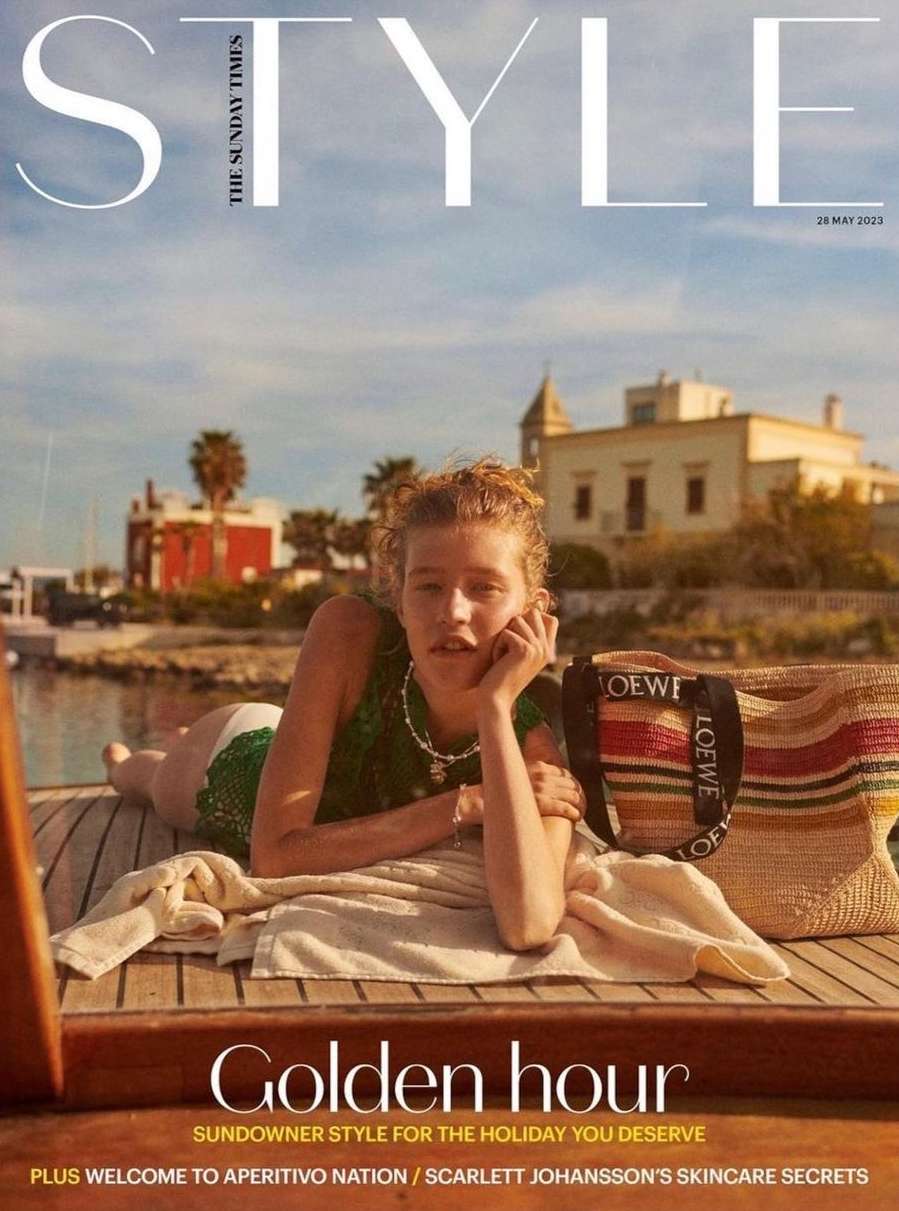 Magazine cover featuring a woman reclining on a boat, showcasing Loewe tote bag, set against a coastal backdrop with clear blue sky.