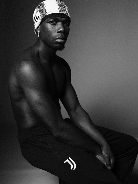 Portrait of adult male athlete posing shirtless in athletic pants and head covering in black and white photo studio environment.