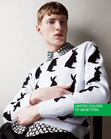 A young man with reddish hair wearing a white sweater patterned with black rabbits and a patterned collar.