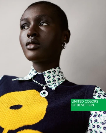 Close-up portrait of a black woman wearing a navy sweater vest over a floral shirt and a silver pendant necklace