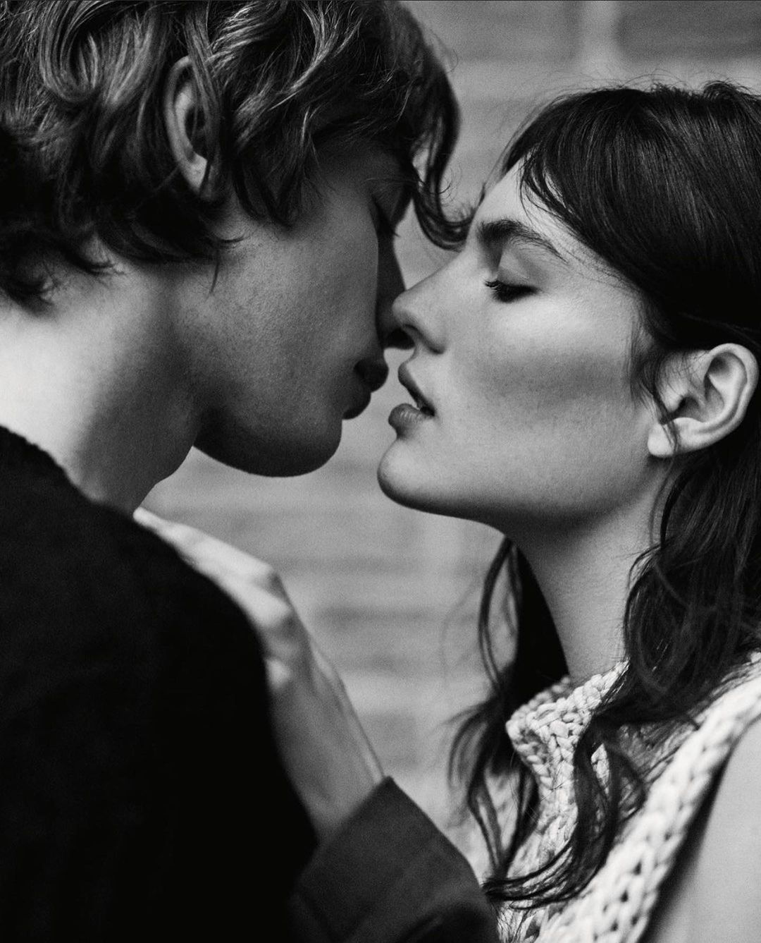 Monochrome portrait of a close-up of a couple in love, intimately close, with soft lighting and a brick wall background.
