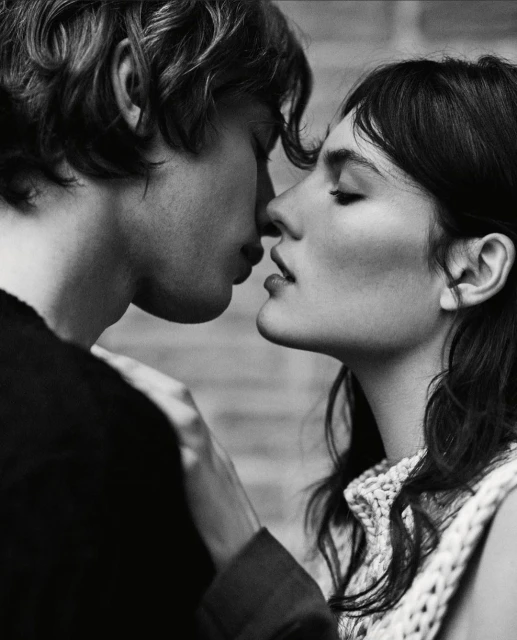 Monochrome portrait of a close-up of a couple in love, intimately close, with soft lighting and a brick wall background.