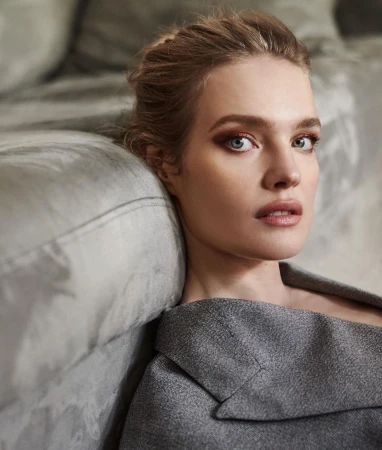 Close-up portrait of a woman resting her head against a grey upholstered sofa wearing a structured grey blazer