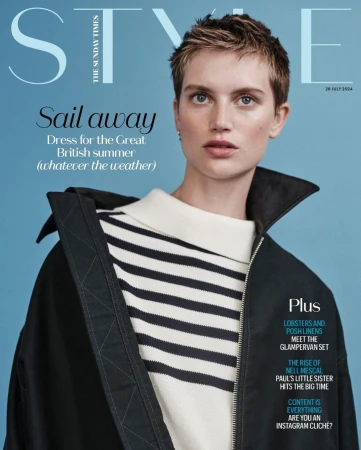 Model with short brown hair wearing a striped sweater and black jacket against a blue background
