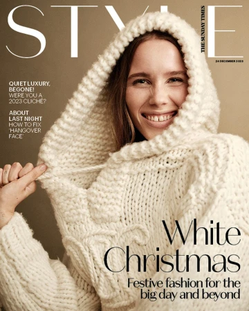 A smiling woman wearing a heavy cream-colored knit hooded sweater against a neutral background, styled as a magazine cover.