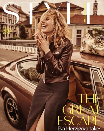 A fashion magazine cover shot featuring a model leaning against a classic car, set against a European street with buildings in the background.