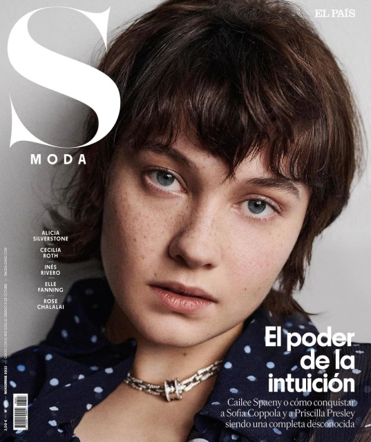 Close-up portrait of a woman with short brown hair and blue eyes wearing a polka dot top and silver necklace for a fashion magazine cover.