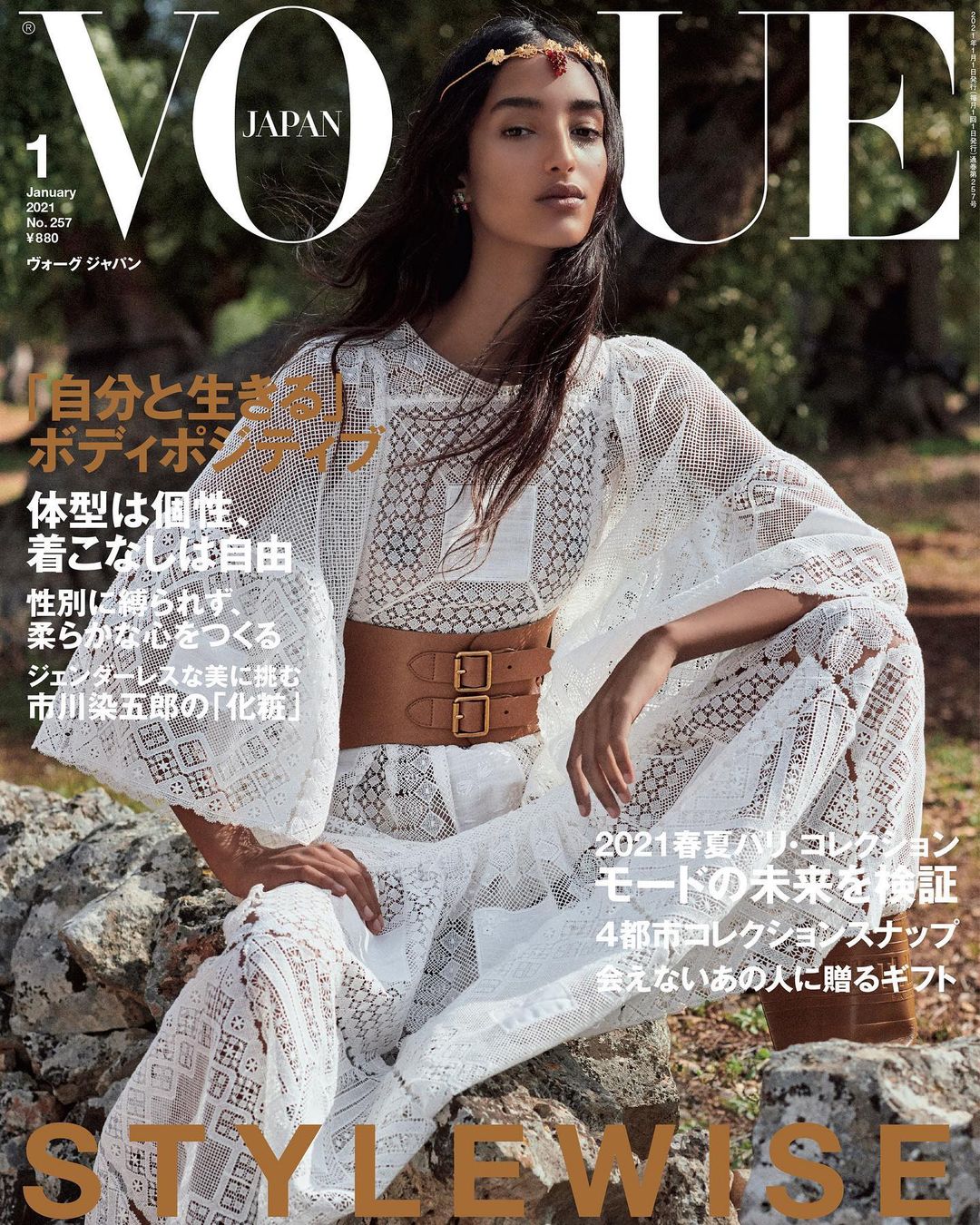 Vogue Japan magazine cover featuring a model in a white lace dress and brown belt sitting on rocks outdoors, showcasing fashion and editorial style.
