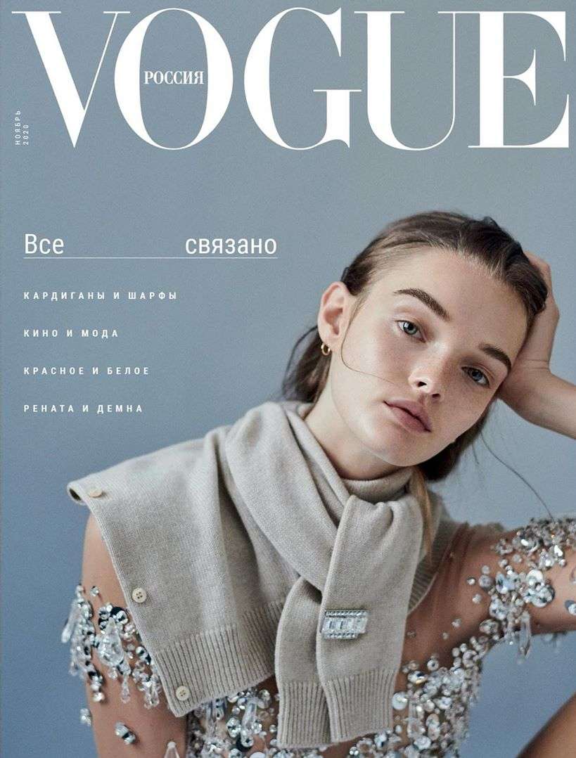 Vogue Russia magazine cover featuring a young adult woman wearing a beige scarf and a sheer embellished dress, with a soft grey background.