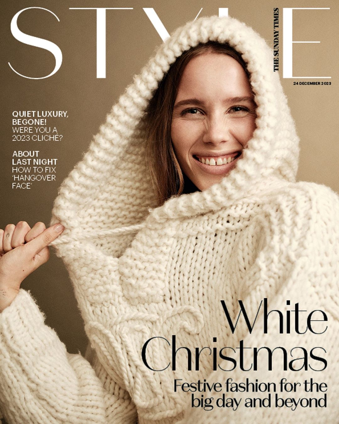A smiling woman wearing a heavy cream-colored knit hooded sweater against a neutral background, styled as a magazine cover.