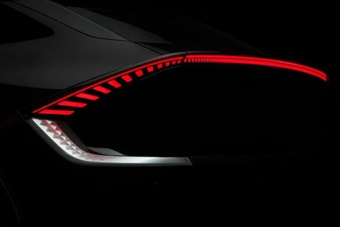 Close-up of a black car's rear, highlighting its modern taillight design with illuminated red and white lights against a dark backdrop.