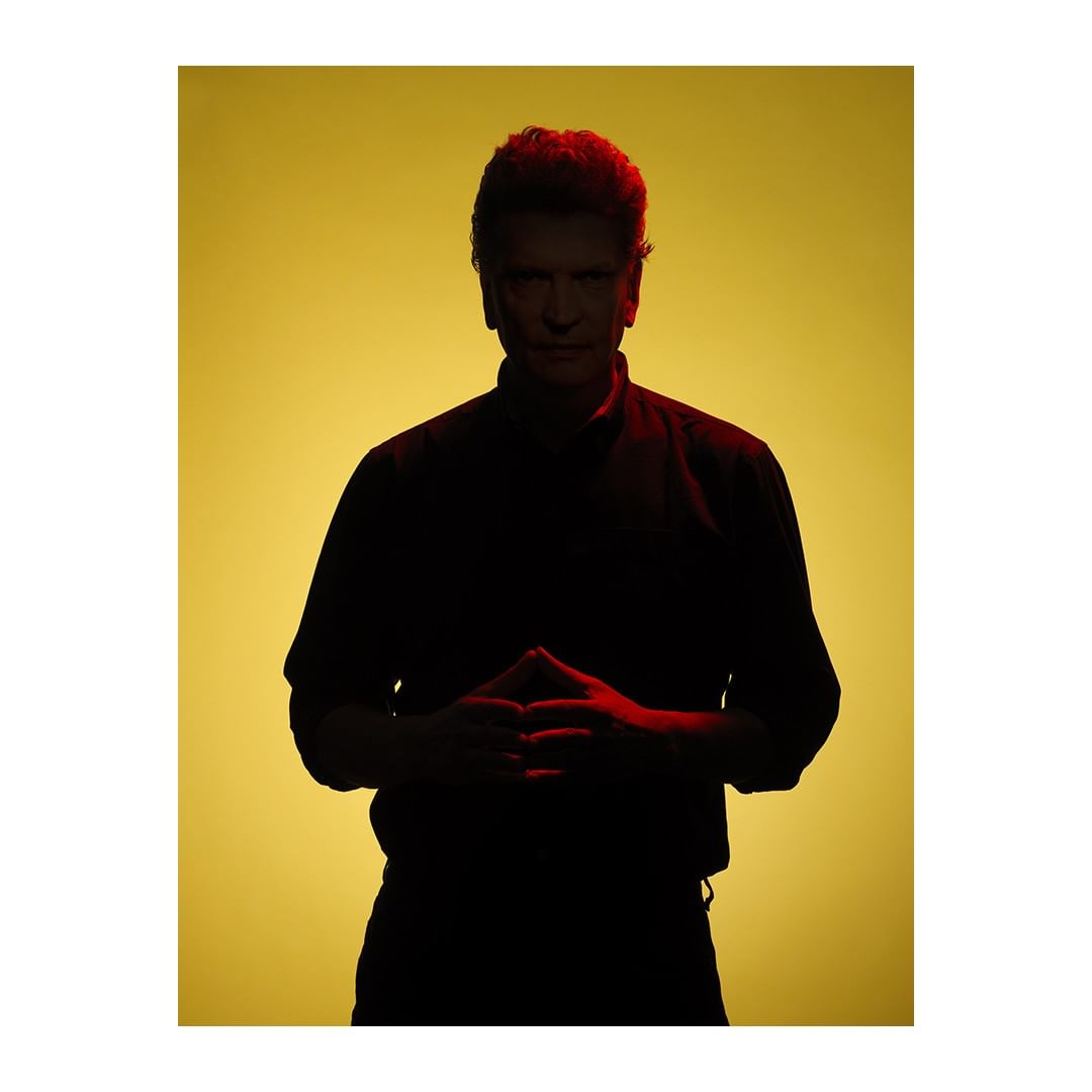 Silhouette portrait of a male adult with hands clasped against a vivid yellow backdrop, captured with dramatic lighting.