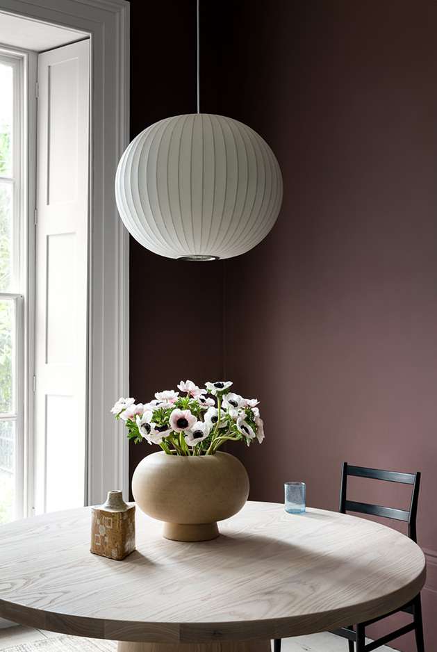 Interior shot of a dining room featuring a round wooden table, a vase with white anemone flowers, and a spherical pendant lamp.