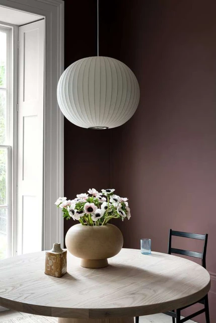 Interior shot of a dining room featuring a round wooden table, a vase with white anemone flowers, and a spherical pendant lamp.
