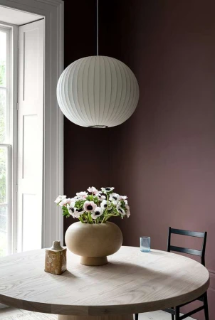 Interior shot of a dining room featuring a round wooden table, a vase with white anemone flowers, and a spherical pendant lamp.