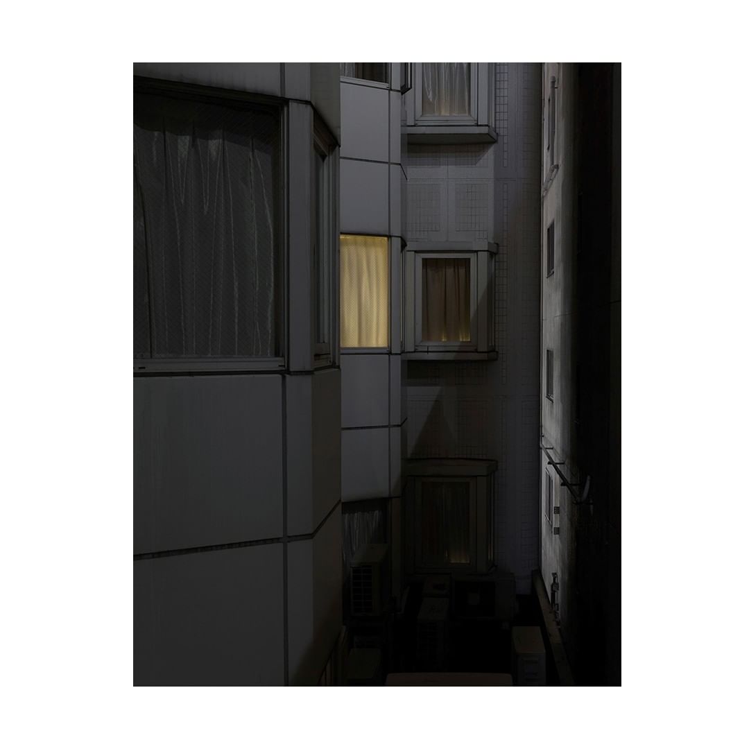 Exterior shot of modern building with multiple windows, one brightly lit at night, creating contrast and highlighting architectural details.