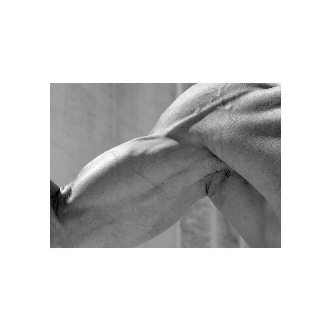 Monochrome close-up of a muscular, flexed arm showcasing muscle definition, veins, and skin texture, against a neutral background.