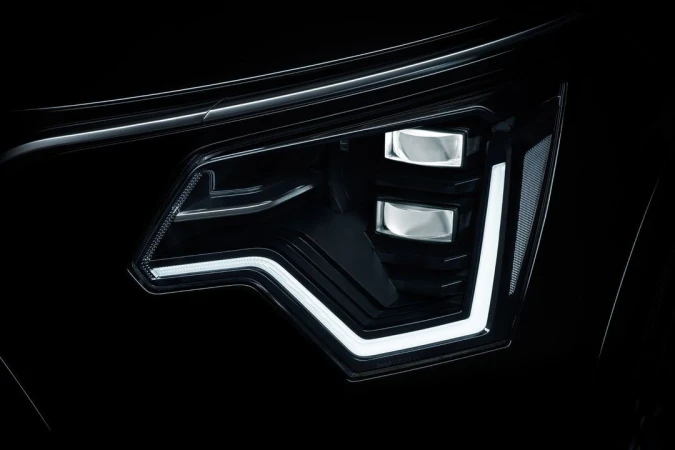 Close-up of an automotive LED headlight with a modern design featuring black housing and geometric patterns of bright white light.