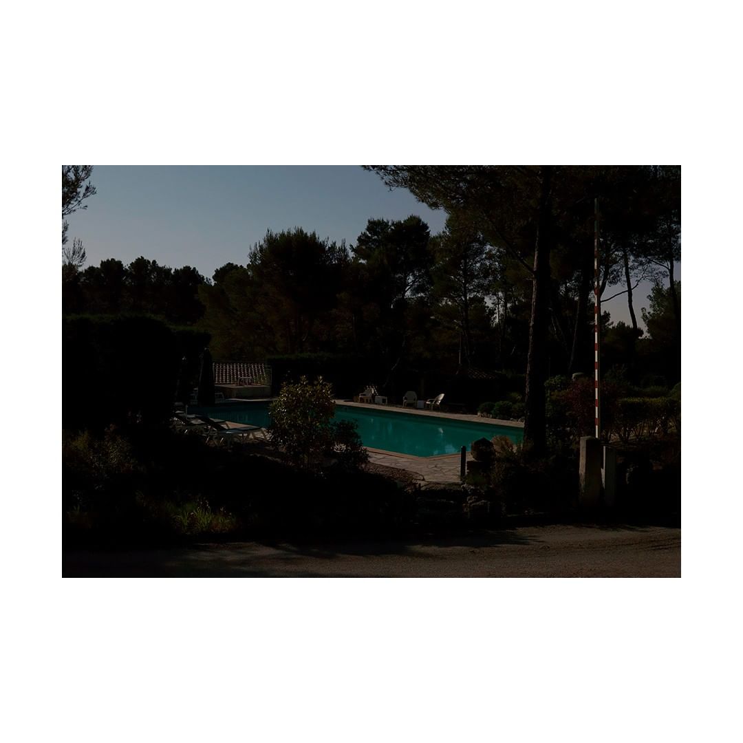 Outdoor swimming pool surrounded by trees on a sunny day, partially obscured by shadows, evoking a secluded and tranquil atmosphere.
